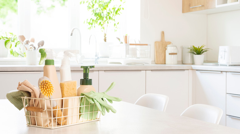 Basket of kitchen cleaning supplies, including spray and scrub brush, on a kitchen table