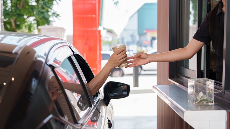 Drive thru employee handing coffee to customer in car