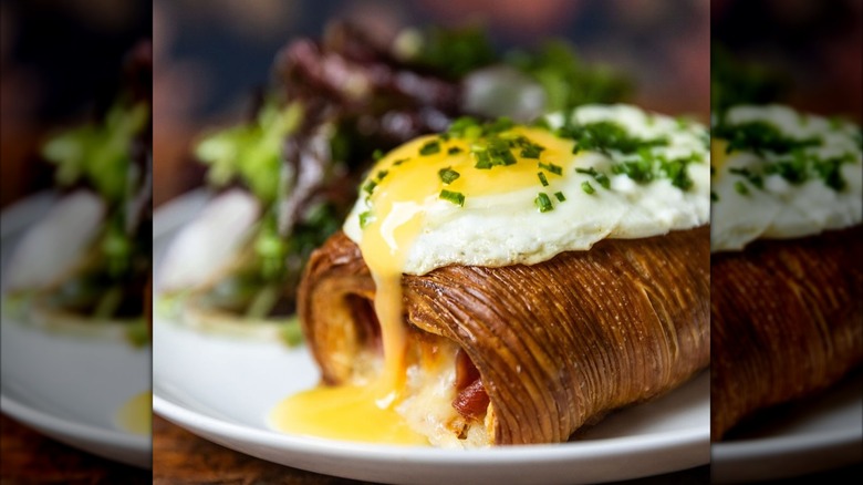 Brunch dish with runny egg, pastry, and greens on plate