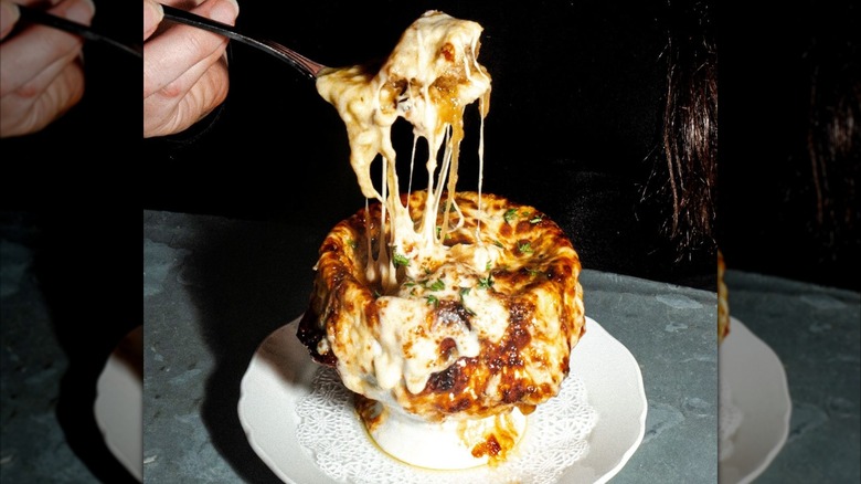 Taking a scoop from bowl of French onion soup with melty cheese
