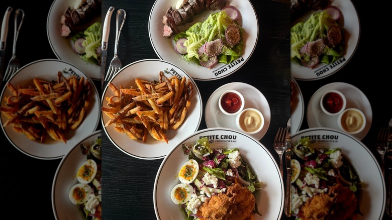 Plates with salads, steak, fries, and dipping sauces on black background
