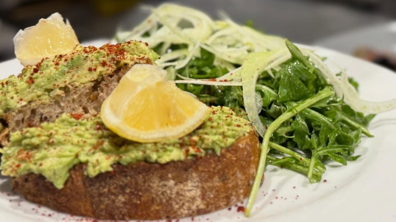 Avocado toast on plate with greens and lemon slices