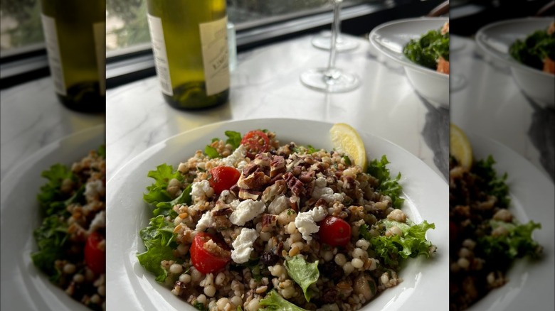 Salad with graims, cherry tomatoes, crumbled cheese, and wine bottle in background
