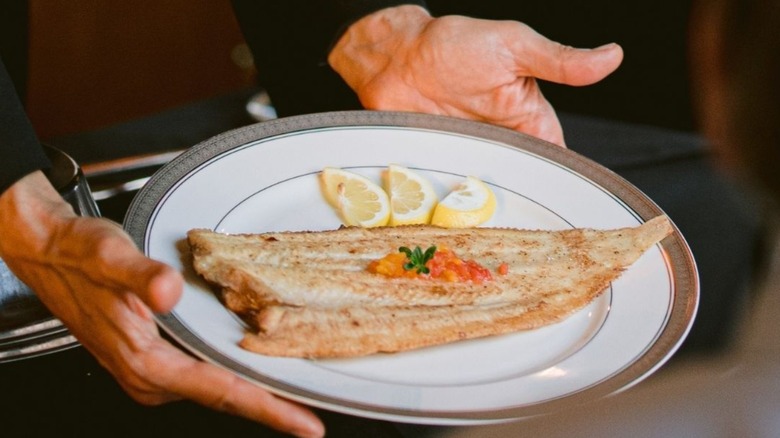 Hands offering a plate with Dover sole and lemons