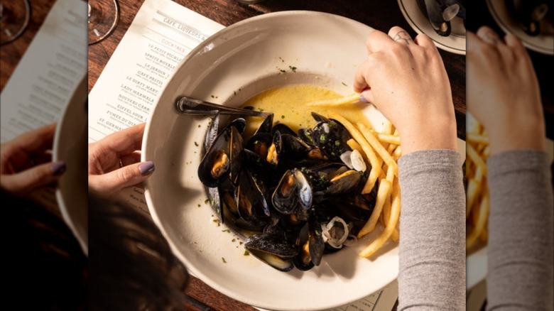 Plate of mussels aerial with hand dipping fry in sauce