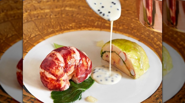 Lobster on plate with cabbage and caviar sauce being drizzled from a spoon