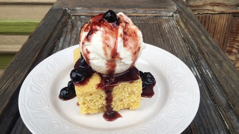 Cornbread topped with blueberry compote and ice cream on a wooden table