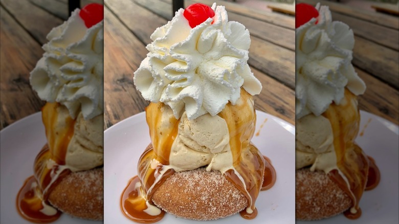 Apple cider donut topped with ice cream, caramel sauce, whipped cream, and a cherry on a white dish