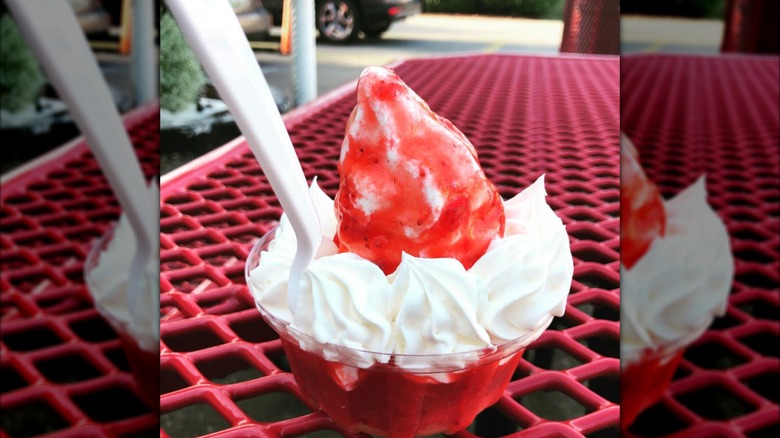 Strawberry shortcake sundae with whipped cream in a plastic bowl on a picnic table