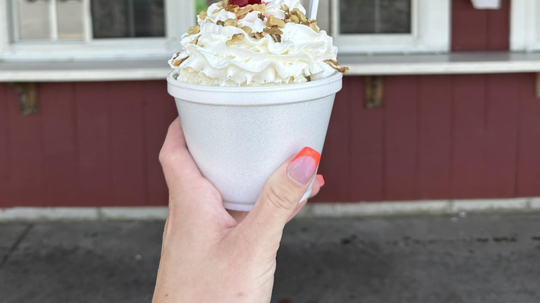 Hand holding blueberry crisp sundae topped with whipped cream, nuts, and cherry
