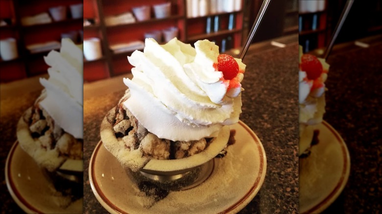 Duster sundae topped with whipped cream and cherry in bowl on plate