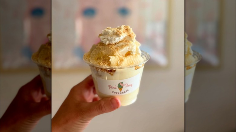Hand holding banana pudding sundae in clear cup with Pink Pony Soft Serve logo