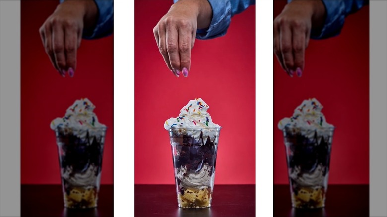 Hand distributing sprinkles on birthday party sundae parfait in clear plastic glass