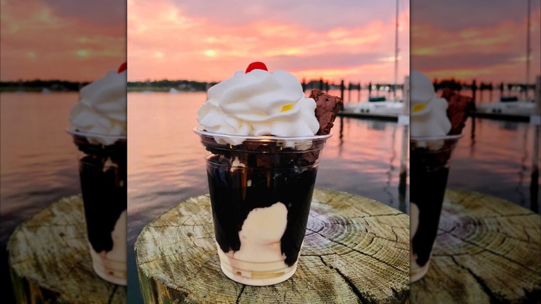 Brownie sundae in clear cup with waterfront at sunset in background