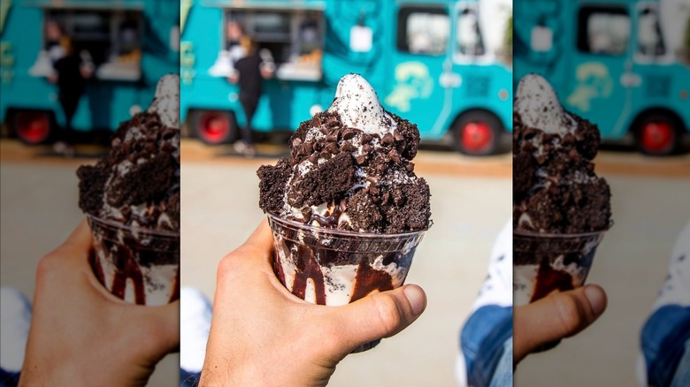 Hand holding sundae covered in Oreo crumbles, chocolate chips, and chocolate syrup in front of ice cream truck