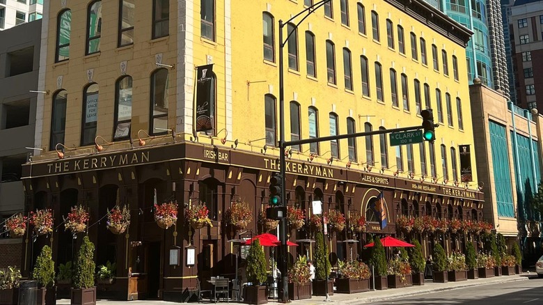 Exterior of The Kerryman yellow and brown building with hanging flower baskets and red umbrellas