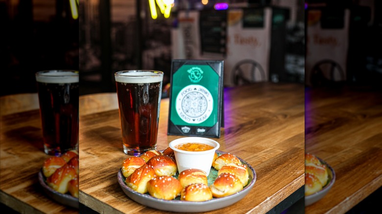 Plate of pretzel bites and cheese dip with pint on wood-grain table