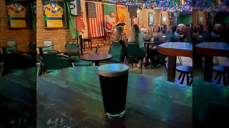 Pint of Guinness on table with stage, musicians, and customers at tables in background