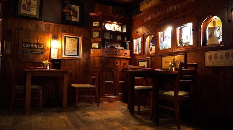 Dimly lit pub interior with tables, chairs, cabinet, and walls with signs and photos