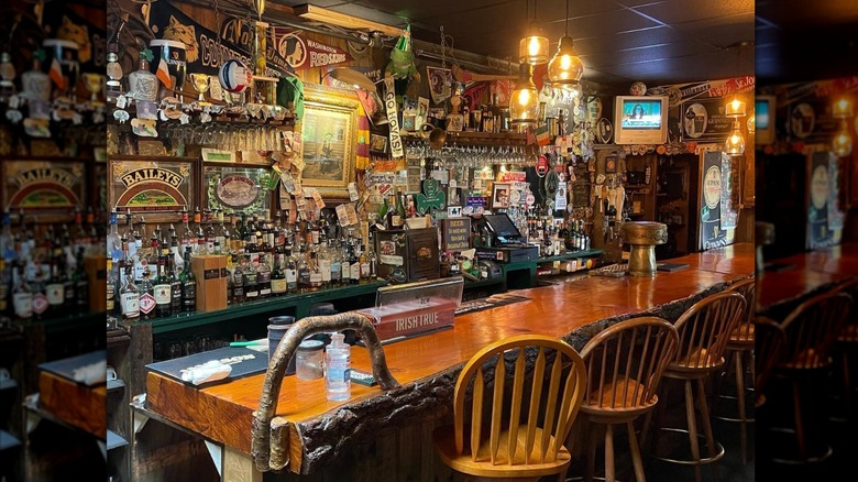 Rough wooden bar with bar chairs and back bar crowded with bottles, signs, and decorations