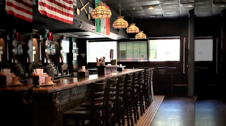 Dark wood bar with chairs, flags, and hanging lights