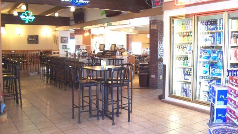 High tables and chairs with bar and coolers of beers in background
