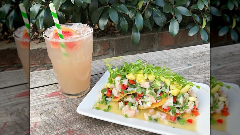 Plate of ceviche and cocktail on wooden table outside