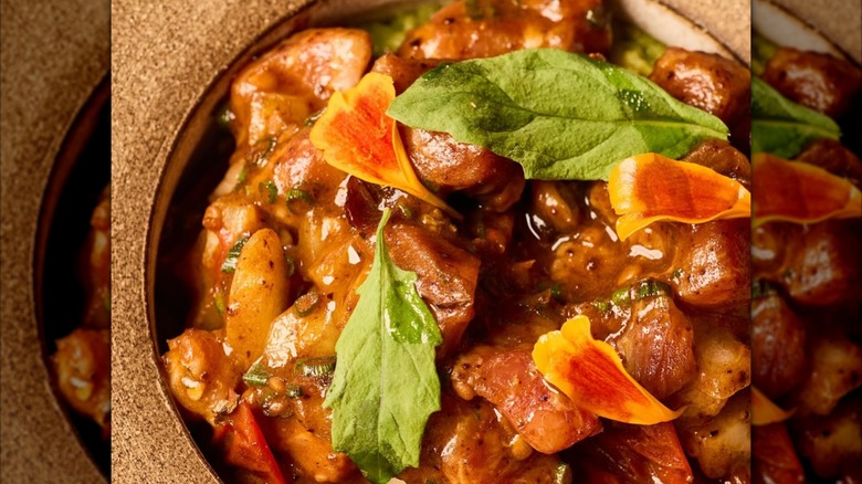 Beef dish with steak and flower petals on brown plate