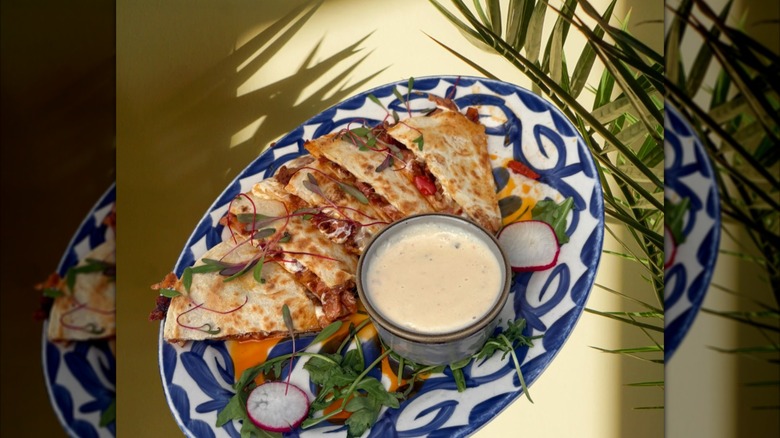Ham, bacon, and cheese quesadilla on plate with palm fronds