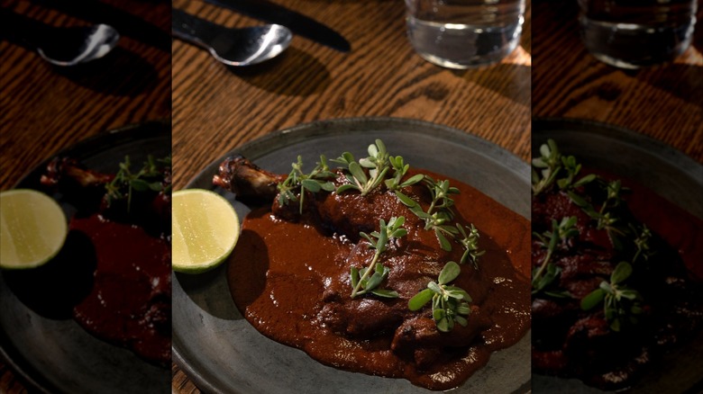 Dish showcasing scratch-made mole with lime and poultry leg on wooden table
