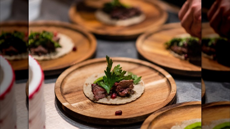 Group of small wooden plates with beef and cilantro dish on a tortilla