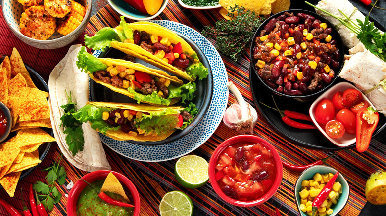 Assortment of Mexican dishes including tacos and elote with limes and peppers