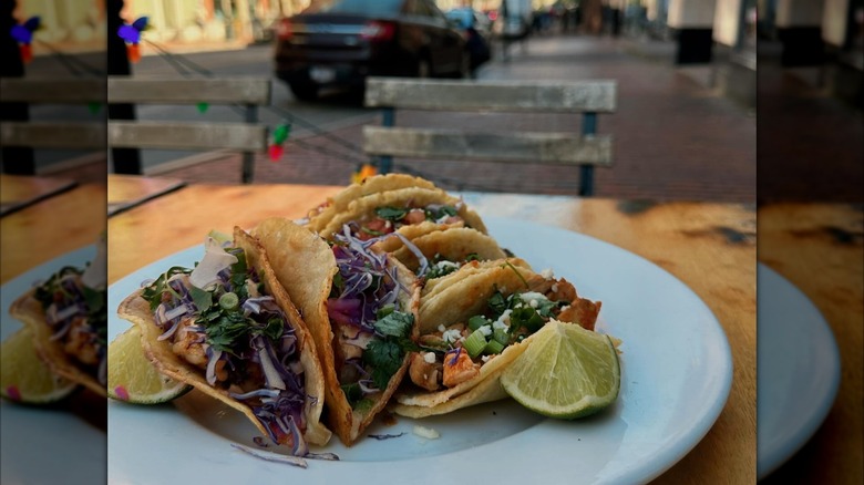Plate of tacos with lime wedges on table on city street