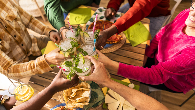 Group clinking mojitos over table with chips and appetizers