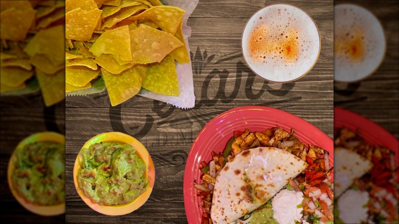 Wooden table with plates of chips, guacamole, and tacos