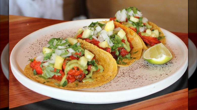 Tacos with fresh pico and guac on white plate with lime slice