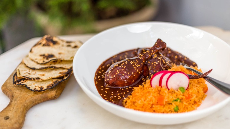 Dish with mole, poultry leg, and rice with side of tortillas