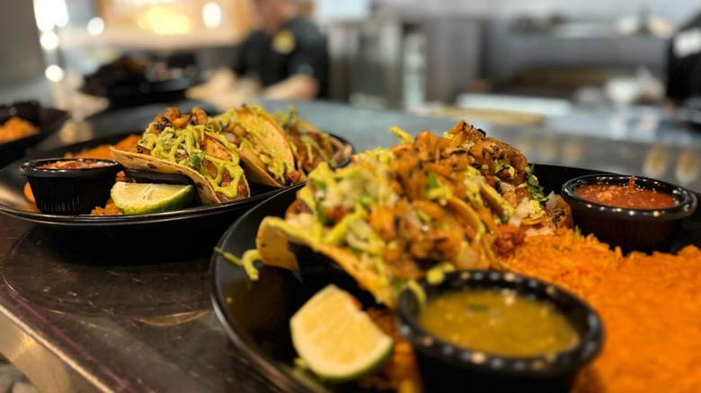 Plates with tacos, rice, salsas, and limes on line to be served