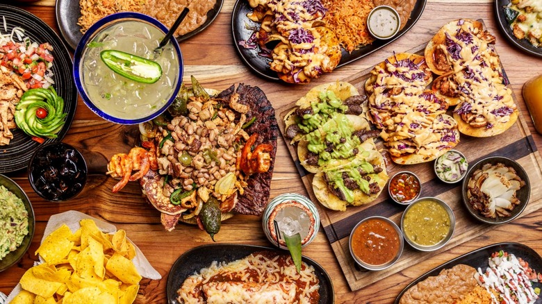 Assortment of Mexican dishes, salsas, and cocktails on a wooden table