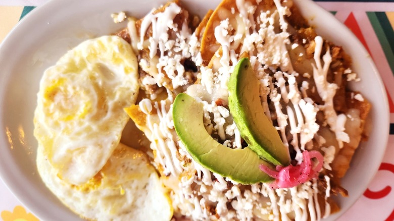 Chilaquiles with sliced avocado, crema, and cheese on plate