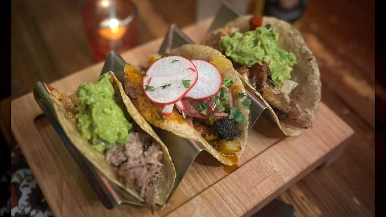Three assorted tacos in taco stand on wooden board