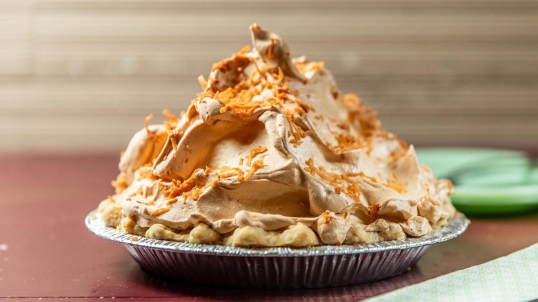 A coconut pie in a tray piled high with whipped cream and toasted coconut