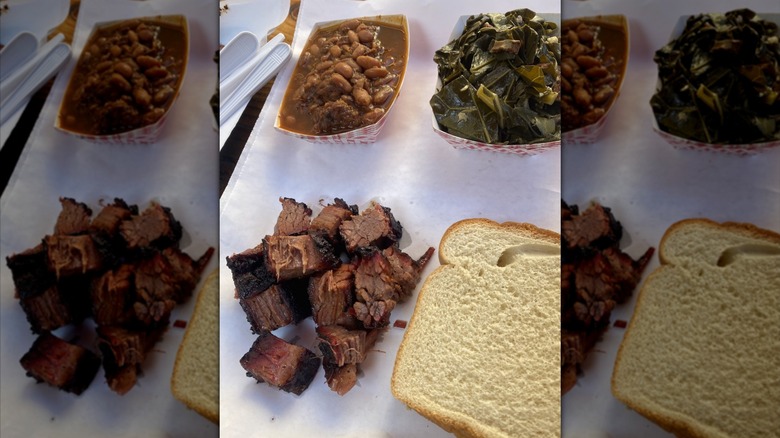 Burnt ends, baked beans, collard greens, and a slice of white bread on a piece of butcher paper.