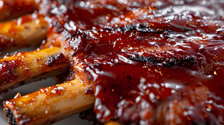 A close-up on a rack of ribs drizzled with red barbecue sauce.