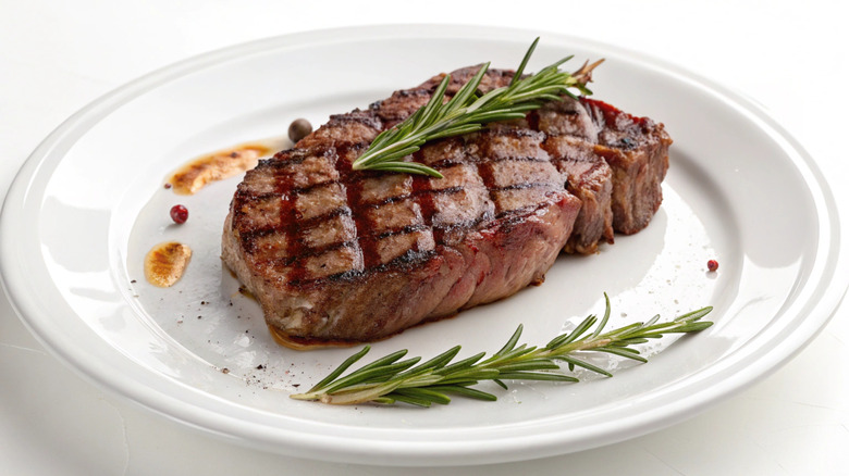 Grilled ribeye steak on white plate garnished with rosemary