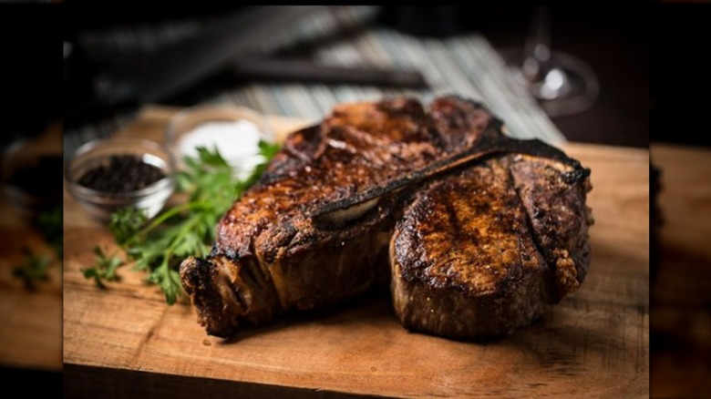 Smith & Wollensky porterhouse steak on a wooden cutting board with vegetables in the back and spices