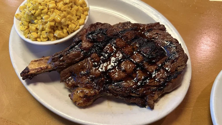 Texas Roadhouse bone-in ribeye with bowl of corn on white plate