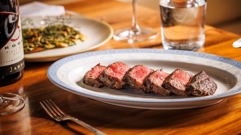 Sliced steak on a plate with utensils on wooden table