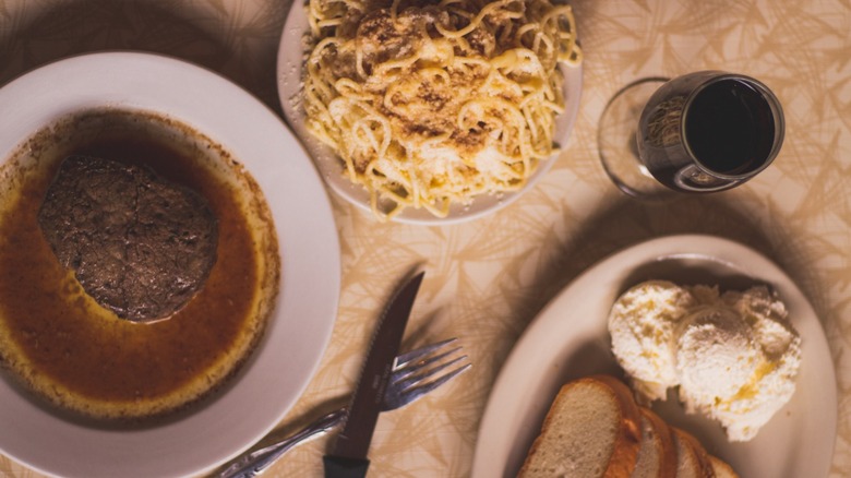 Juicy beef filet with Greek spaghetti, plate of bread, and glass of wine top-down