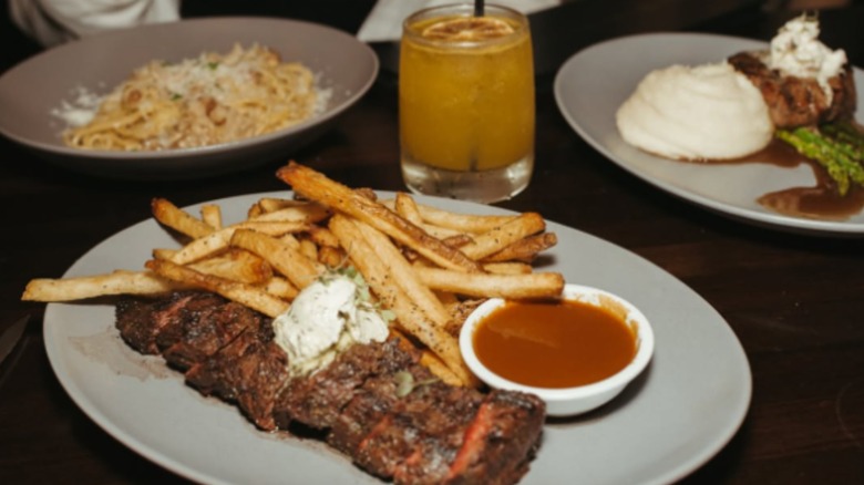 Steak frites on plate with other dishes and cocktail in blurred background